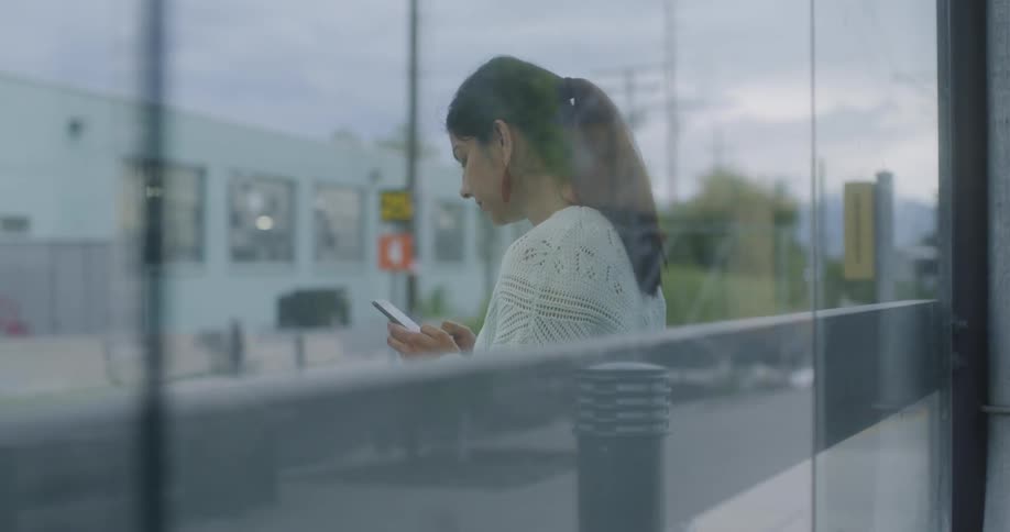The woman checks her phone by the train station