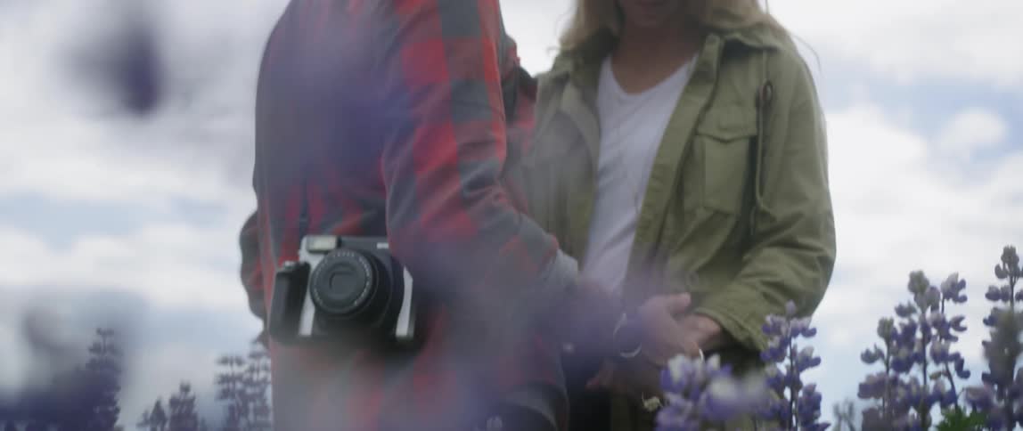 The man and woman hold hands in the field of flowers