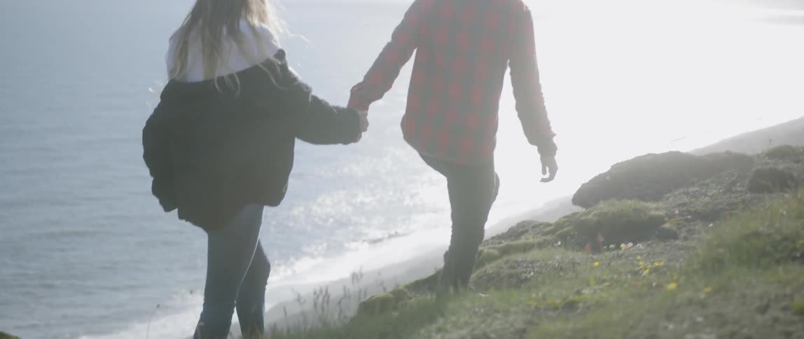 A man and woman walk on the grassy hillside