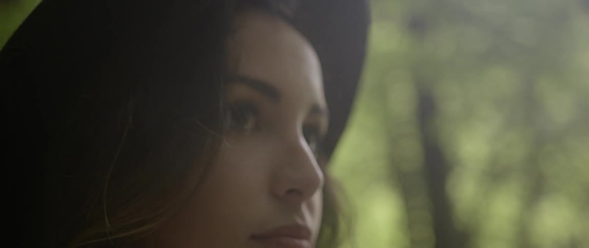 A woman wears a hat in a sunny forest