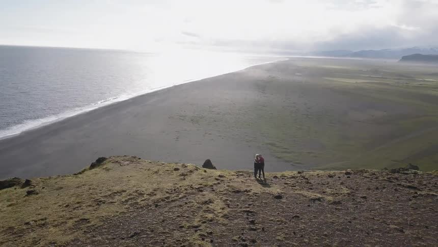 Two people hug on top of the hill by the shore
