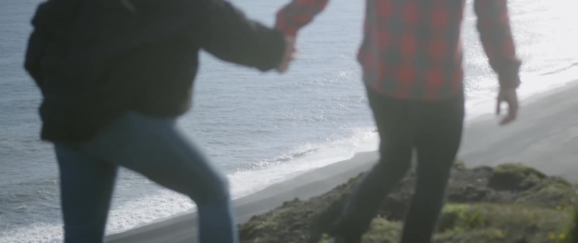 A man and woman hold hands while walking on a beach