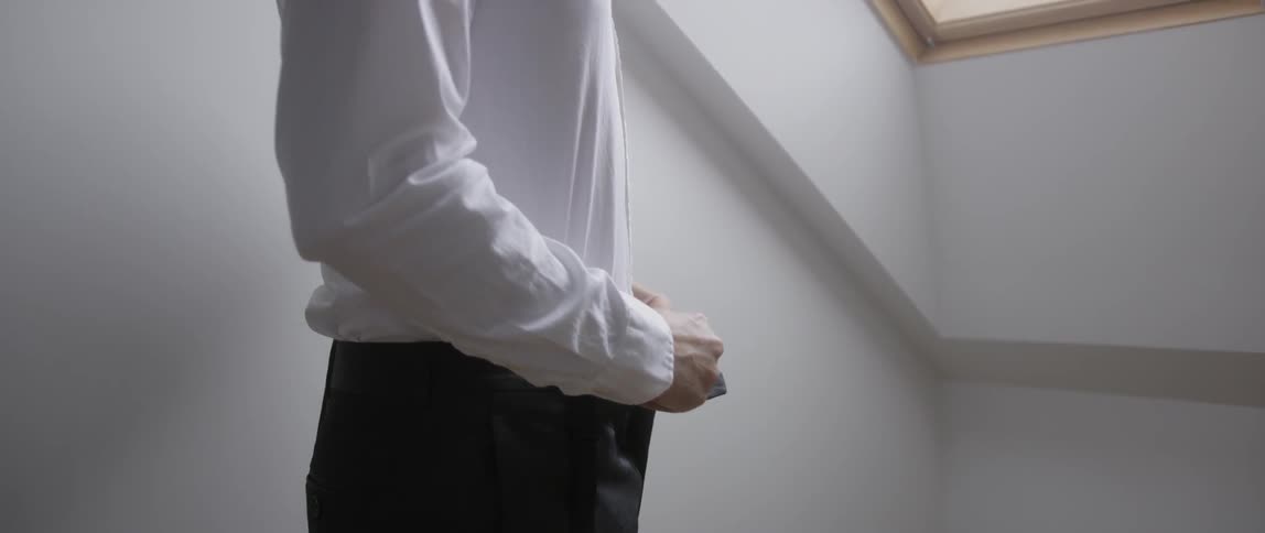 A man buttons up his pants next to an attic window