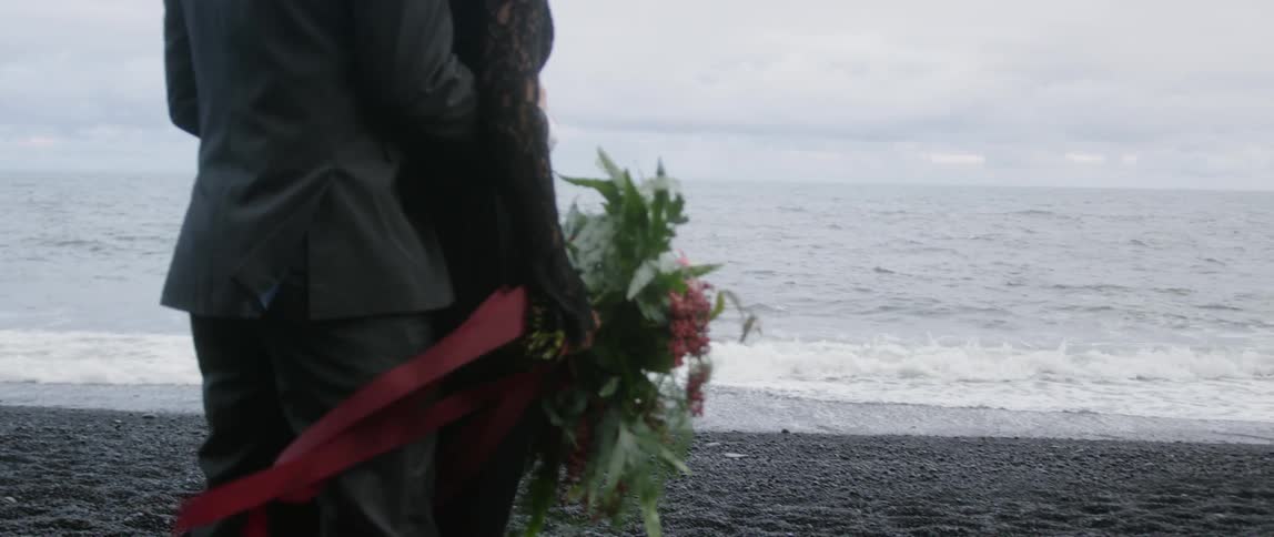 A man and woman stand on a beach with a bouquet of flowers