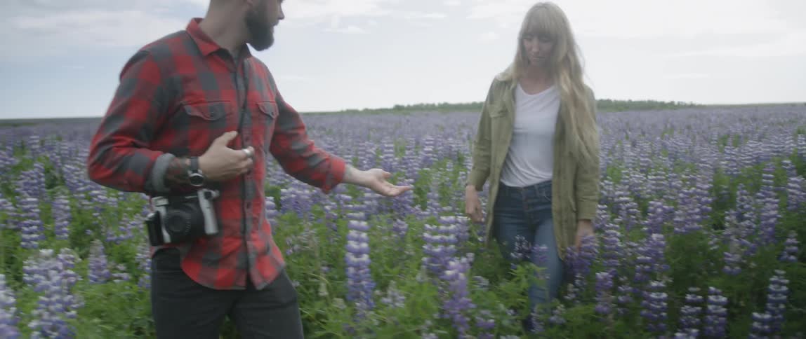 A man and woman walk in a meadow with purple flowers
