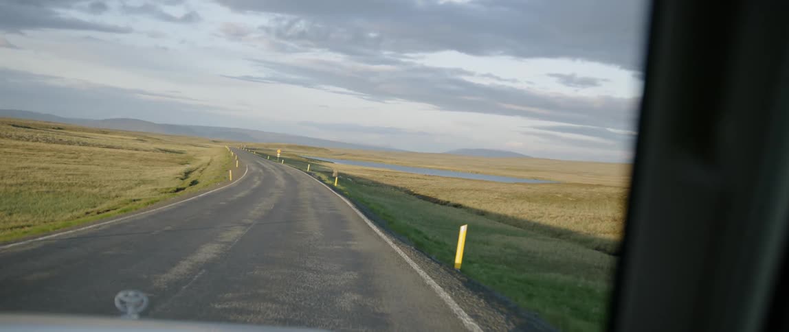 A vehicle drives on a rural road on a cloudy day