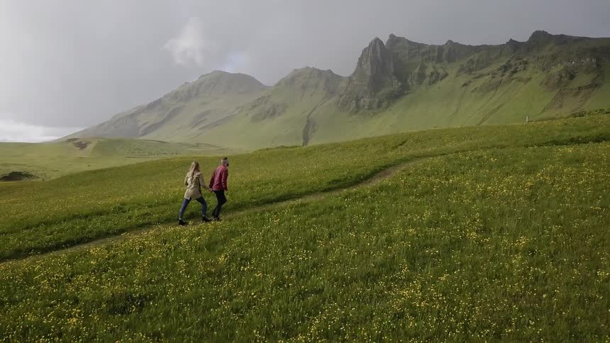 A man and woman walk up a grassy hill