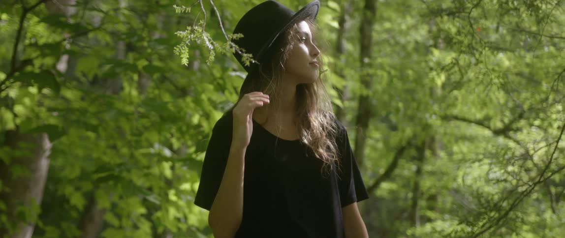 A woman wears a hat in a forest