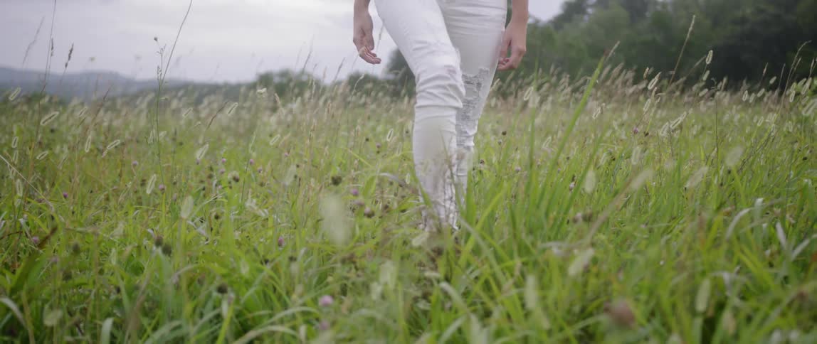 A woman walks in a grassy meadow