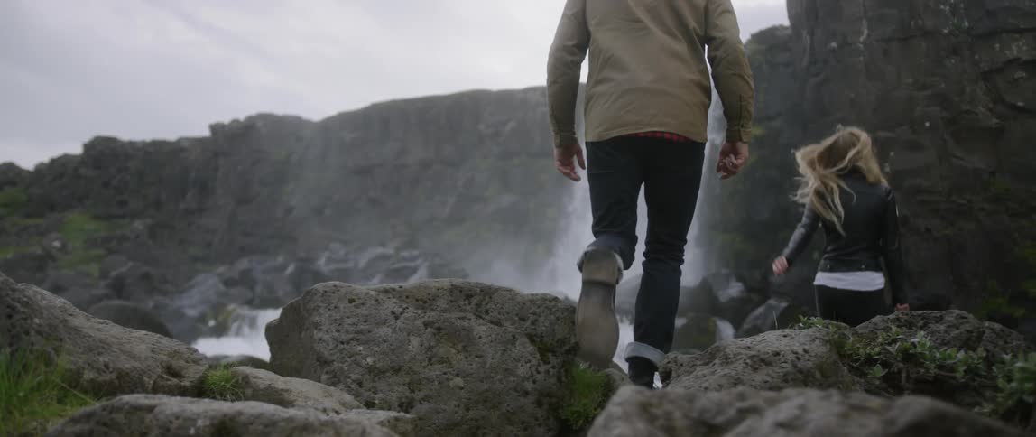 The two people climb over the rocks towards the waterfall