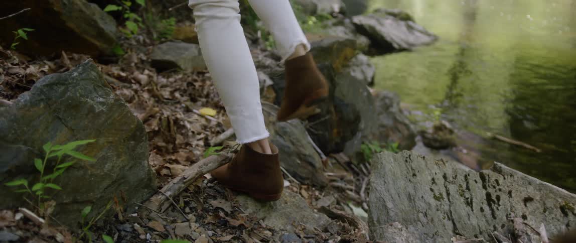 A woman walks over rocks next to a river