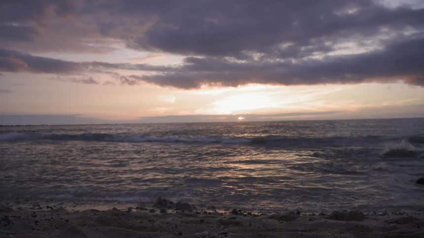Clouds float above ocean waves at sunset