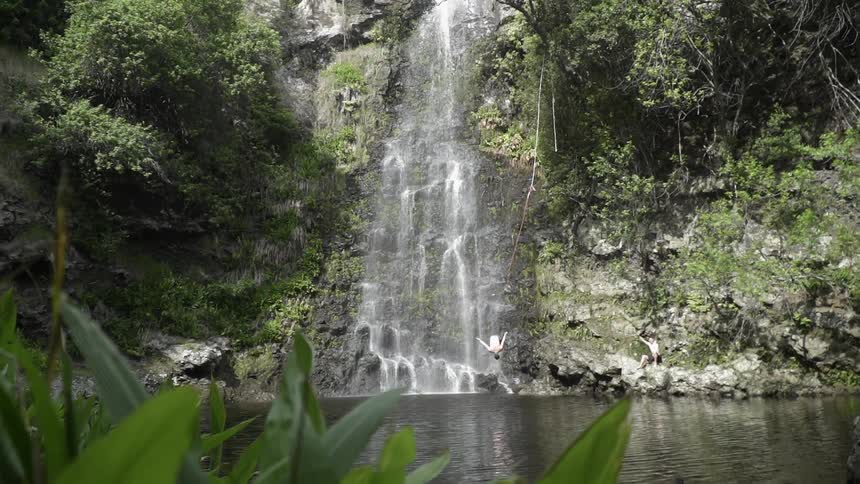 Man swings into the water under the waterfall