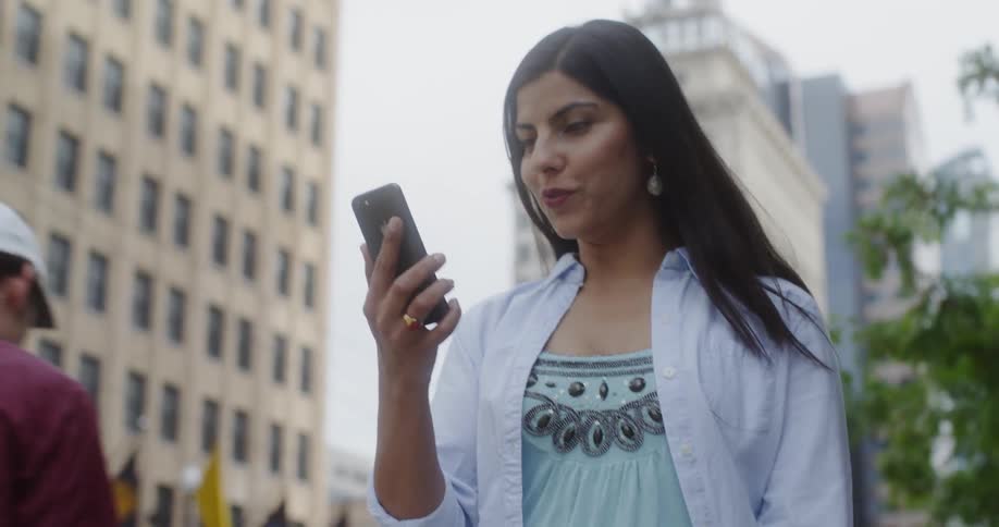 A woman looks at her phone while walking on a city sidewalk