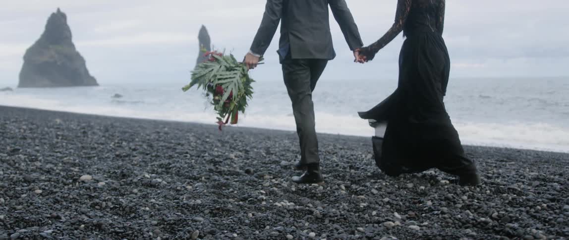 A man and woman walk on the grey beach