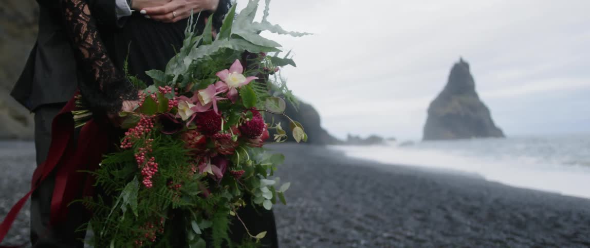 A man and woman stand on a beach with a bouquet of flowers