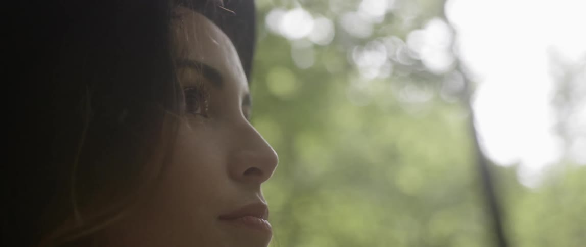 A woman wears a hat outside near trees