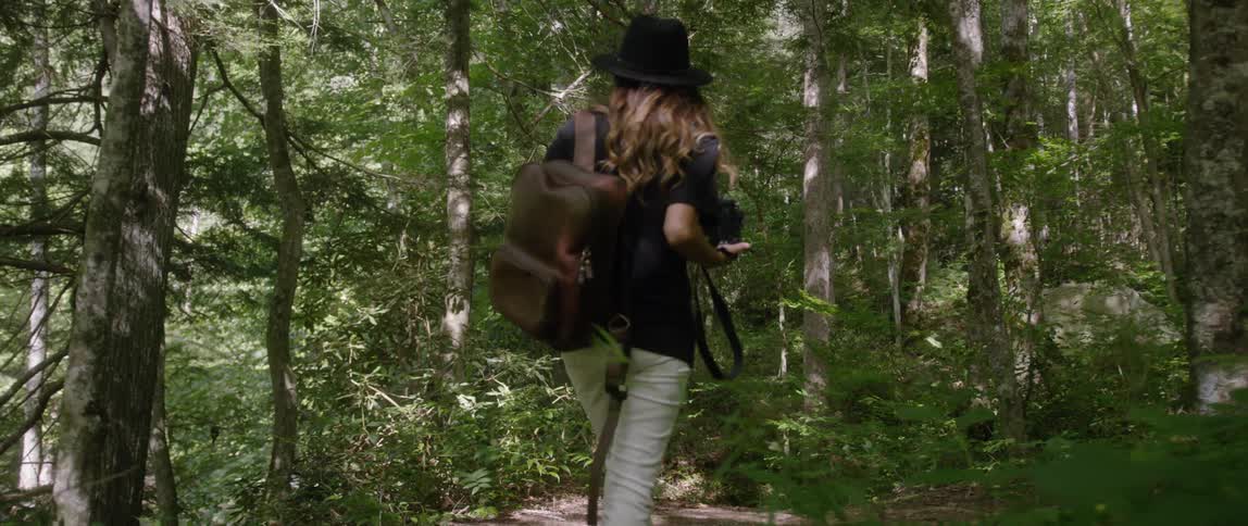 Woman wearing backpack is hiking in forest area