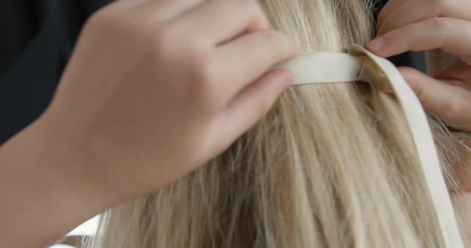 A blonde woman ties a ribbon with beads on it behind her head