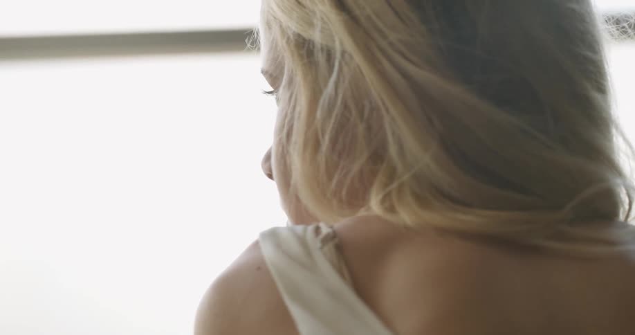 A blonde woman looks out of a window