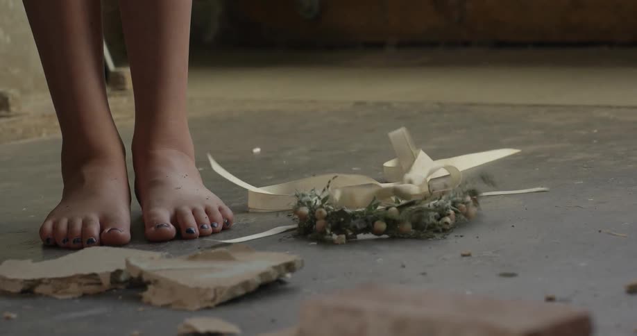 A person standing barefoot on a concrete floor drops their crown of flowers