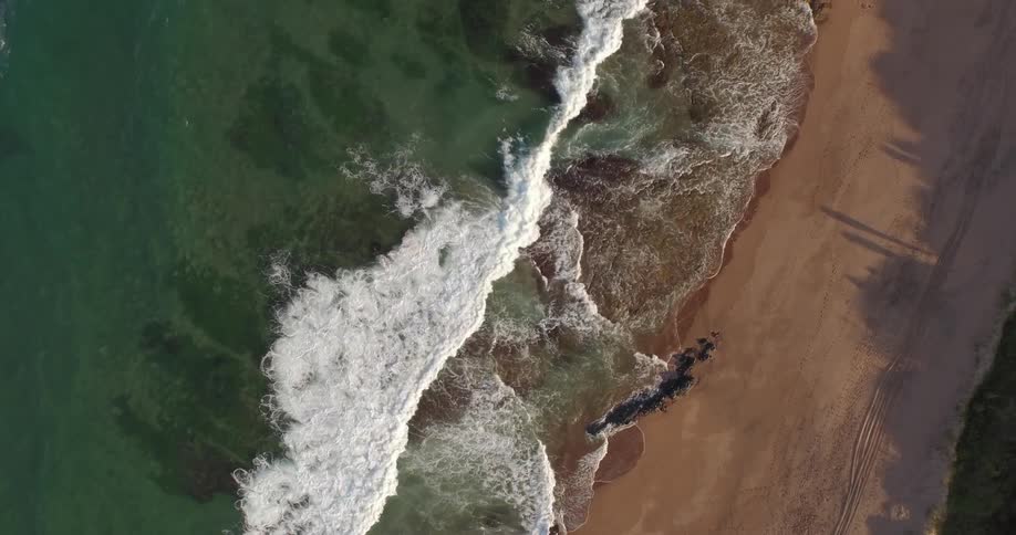 Overhead aerial view of waves crashing on an empty beach