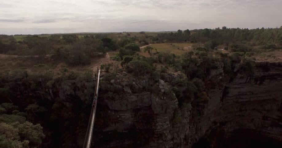 A group of people are walking across a ravine on a rope bridge