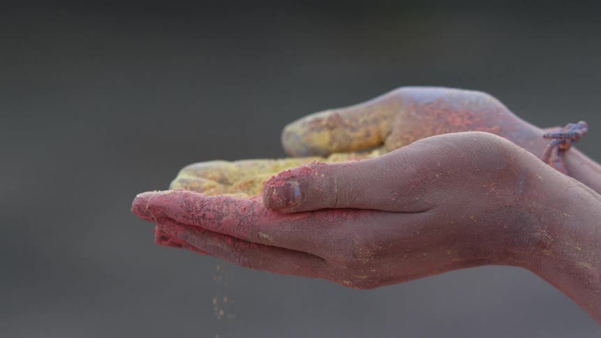 A woman holds yellow and pink powder in her hand