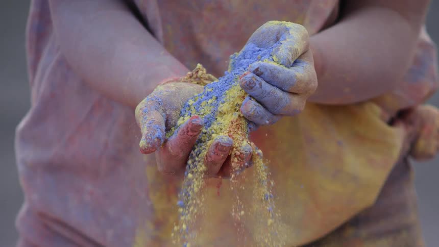 The person tosses colored dirt in their hands