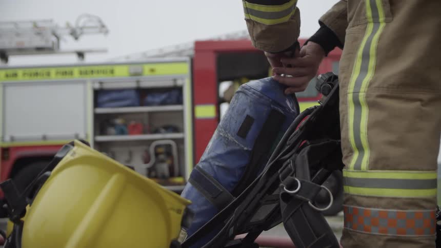 Fireman unscrews a tank from straps by a firetruck