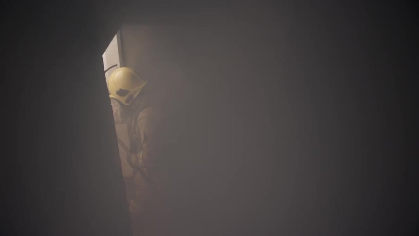 A firefighter enters a smoke filled room