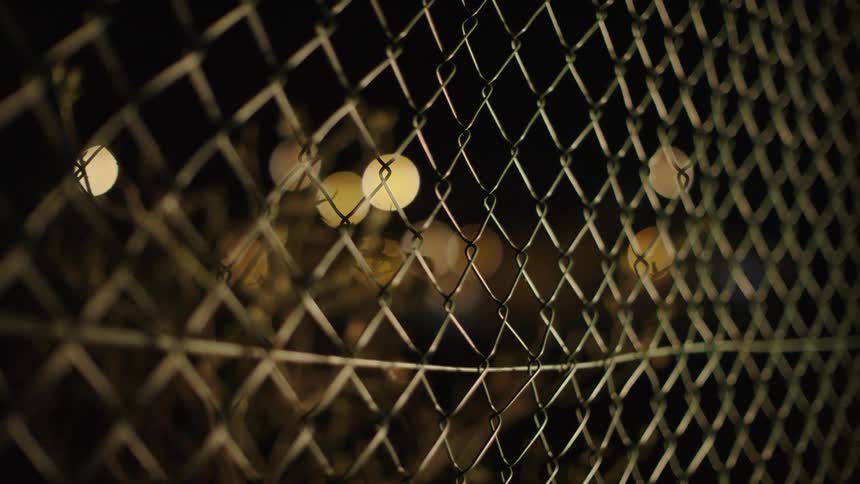 A person walks by a chain link fence at night