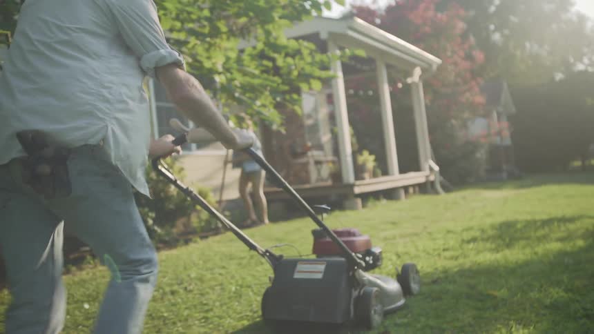A man mows a front lawn on a sunny day