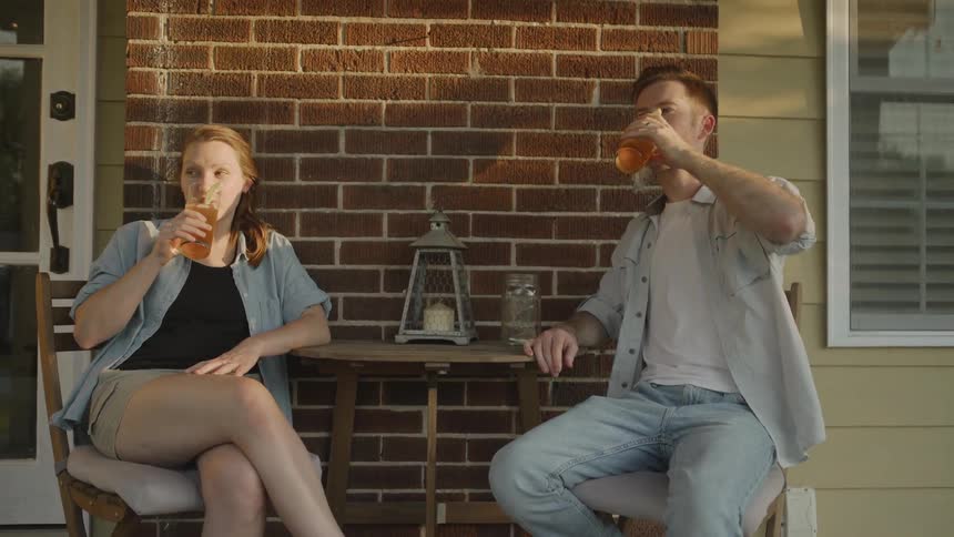 The man and woman take drinks at the table outside