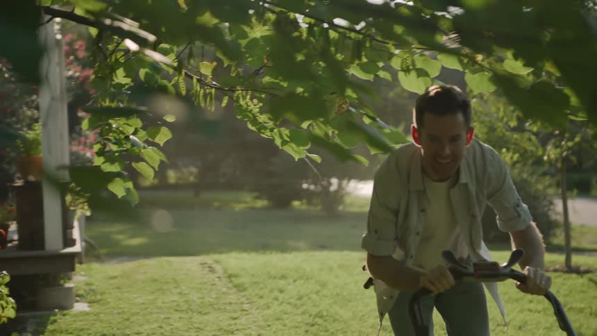 The man pushes the lawnmower in the yard