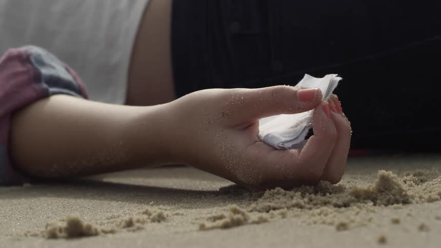 The person is holding a note in the sand