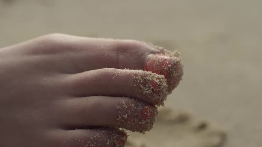 A woman wiggles her sandy toes on a beach