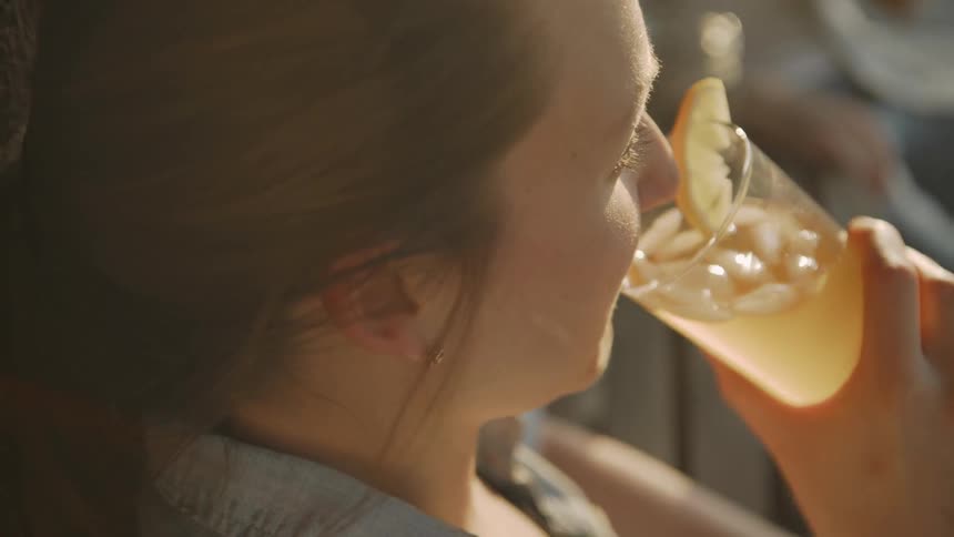 Woman sips out of a glass while sitting on the porch with another person
