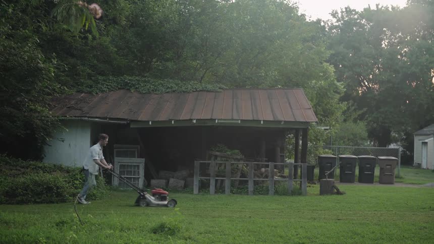A man mows a lawn next to a shed