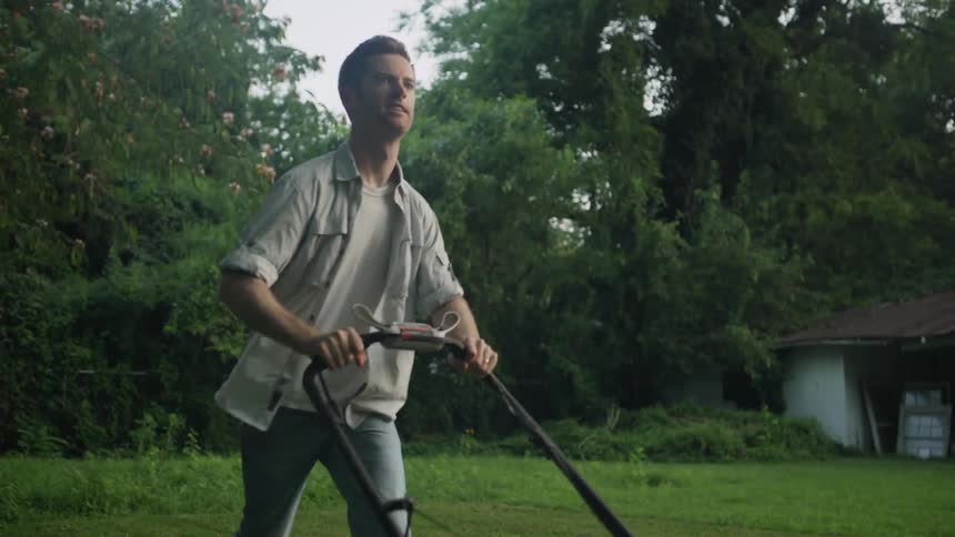 A man mows a lawn with a push lawnmower