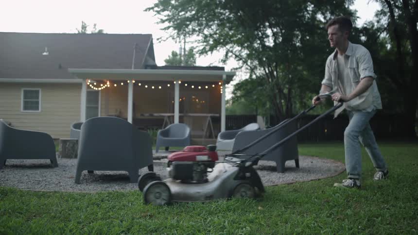 The man is mowing the lawn in the yard
