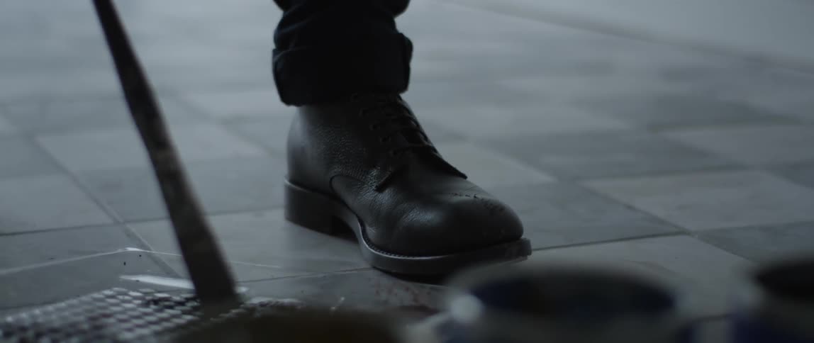 Man in black boots pokes at something on the ground with a stick