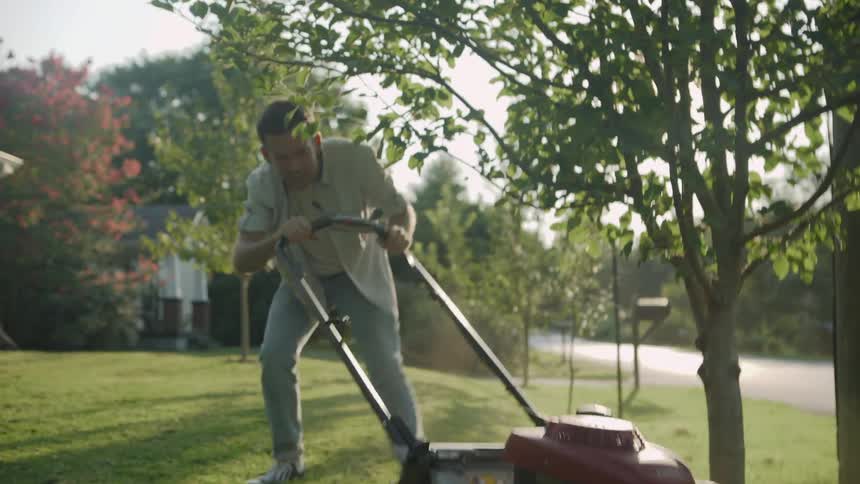Man mows the lawn ducking under a small tree