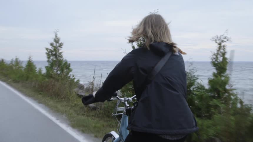 Woman rides on a bike on a road next to the water