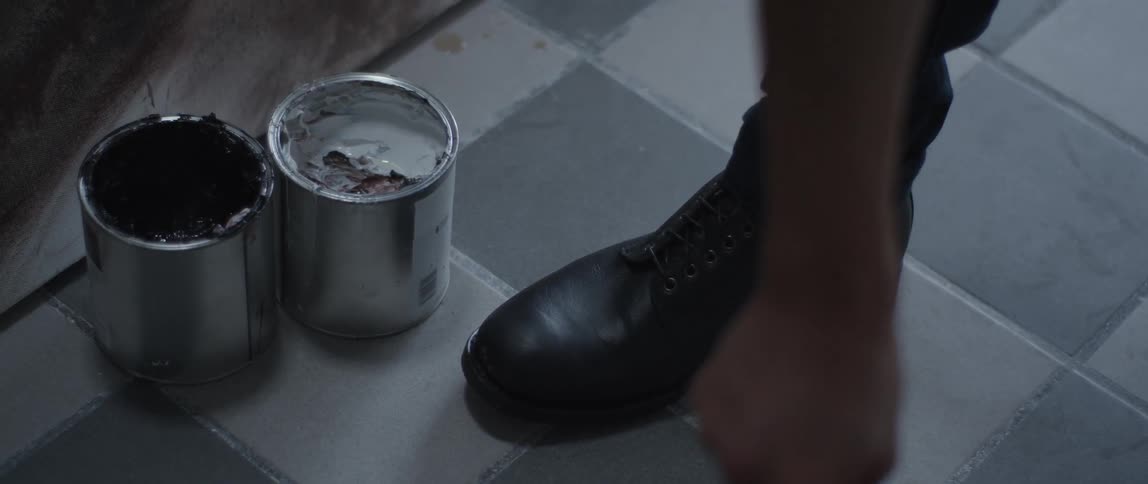 A man dips a paint brush into paint cans on the floor
