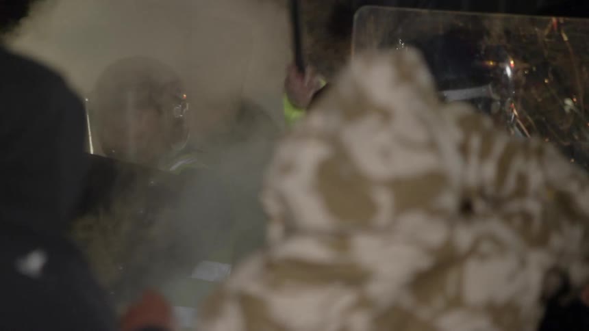 Guards holding shields try to fight off a mob