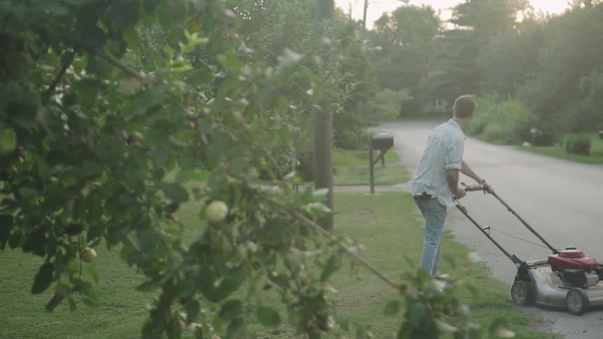 The man pushes a lawnmower by the small road