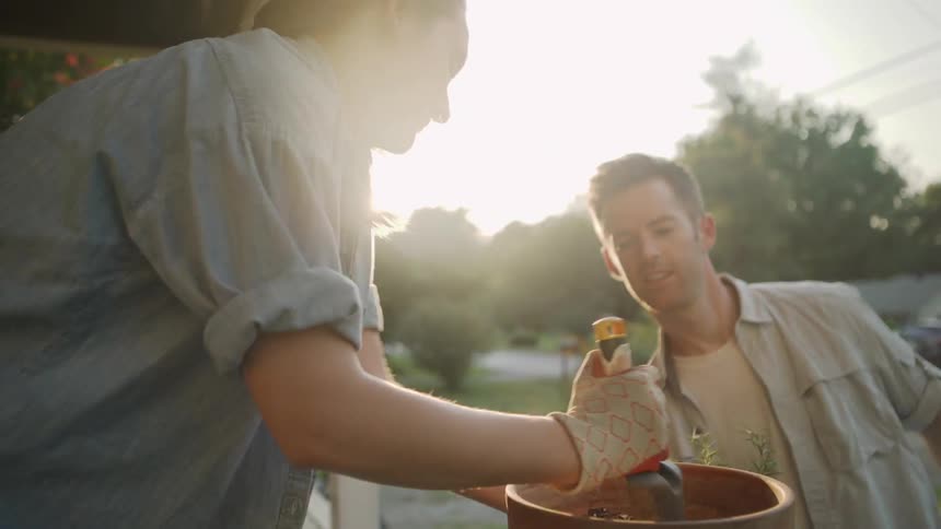 Woman Digs in Flower Pot and Man Picks up a Plant