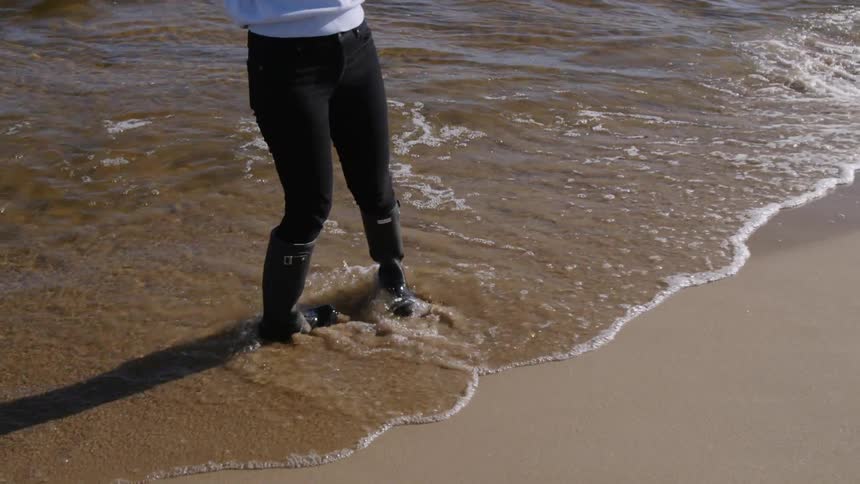 The woman walks around holding a camera on the beach