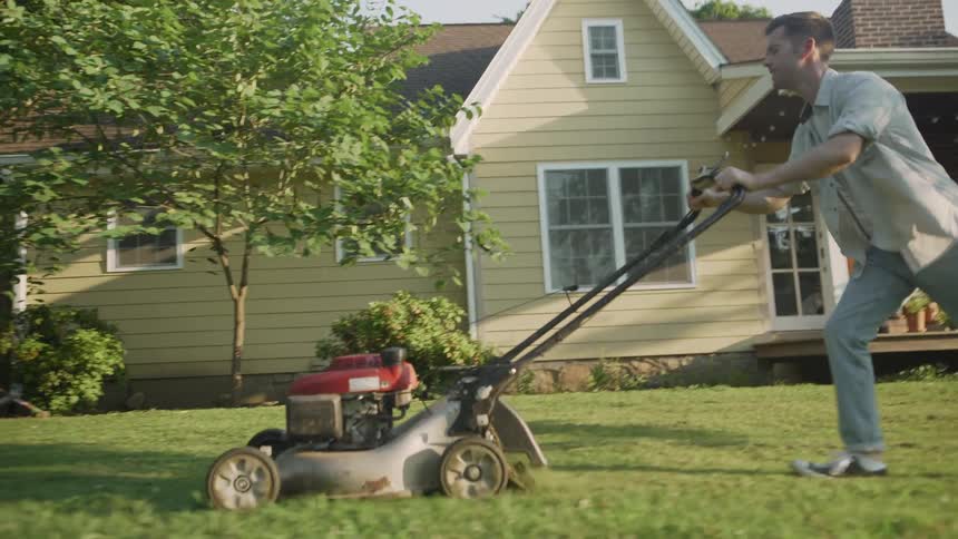 The man is pushing the lawnmower in the grass